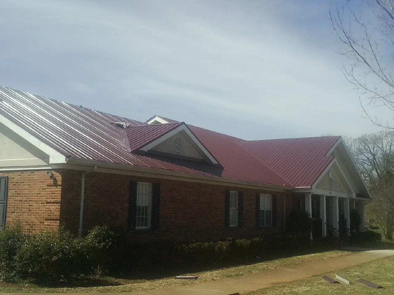 Red metal roof with gabled entries on a long brick building, from a Hail Damage Roof Repair job in Indialantic