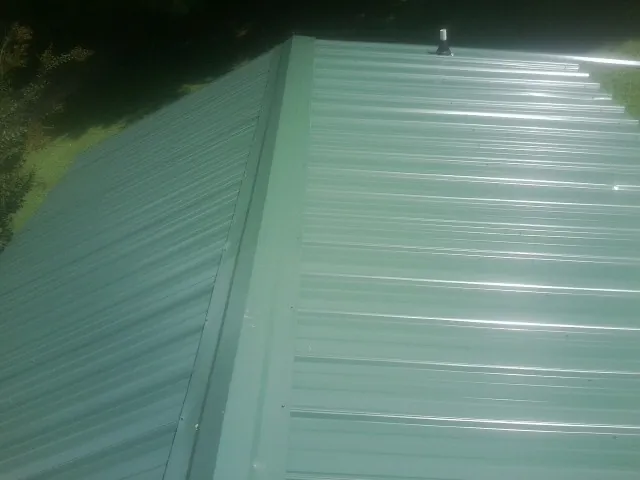 New green metal panels meeting at the ridge of a roof — Flat Roof Repair work by our crew in Indialantic