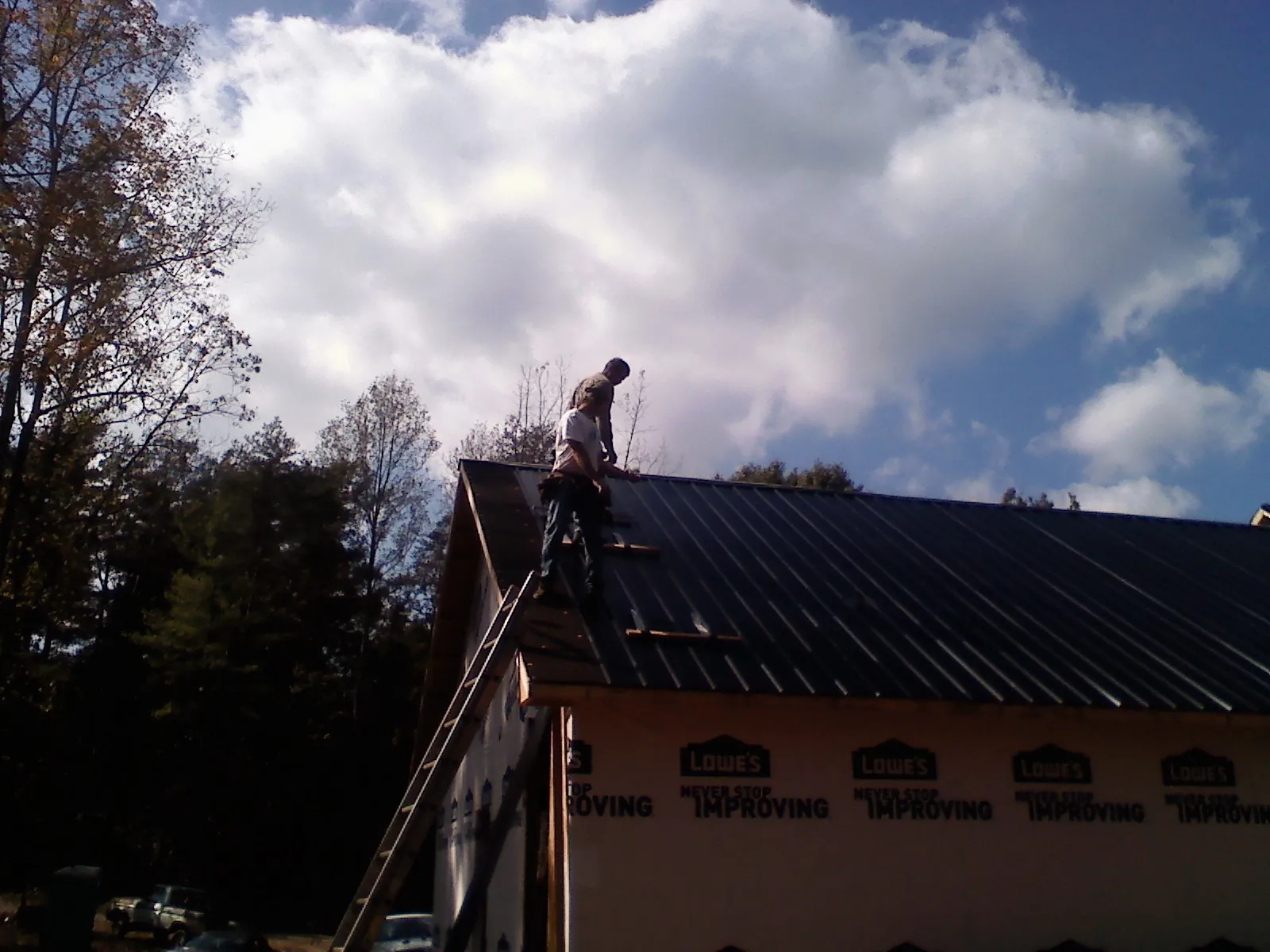 Roofer fastening dark metal panels high against a cloudy sky, from a Roof Inspection job in Indialantic