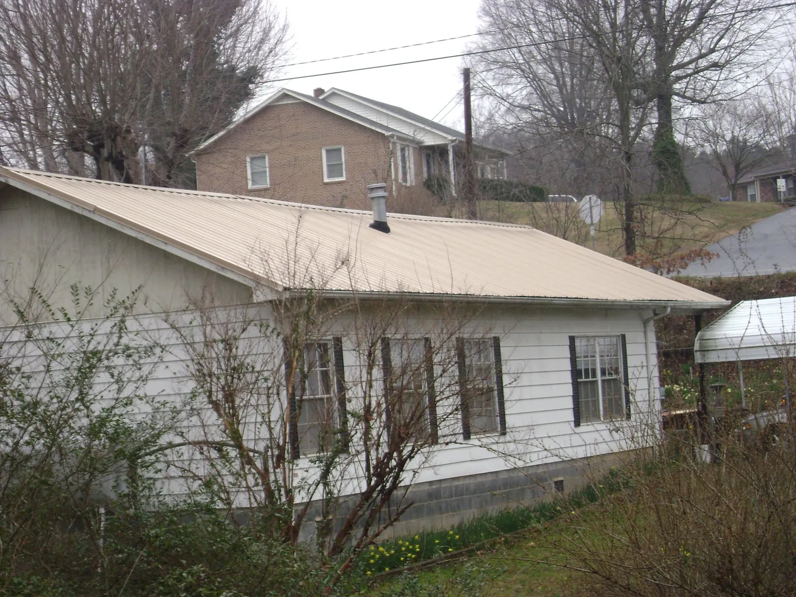 Tan metal roof on a white sided house set into a hillside — Commercial Roofing by Roofing Brothers in Indialantic